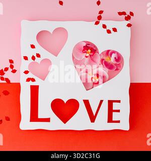Romantic paper cut love sign with flowers and red lips on pastel pink and red background. Love concept with heart shapes and orchids. Flat lay style. Stock Photo