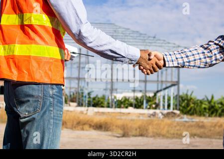 Close up handshake of two engineers on produce site. Group of industries workers meet on manufacture site shake hands Stock Photo
