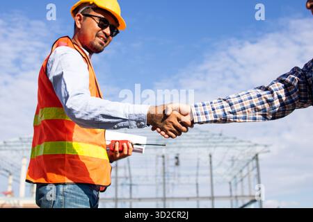 Close up handshake of two engineers on produce site. Group of industries workers meet on manufacture site shake hands Stock Photo