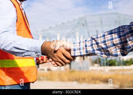 Close up handshake of two engineers on produce site. Group of industries workers meet on manufacture site shake hands Stock Photo
