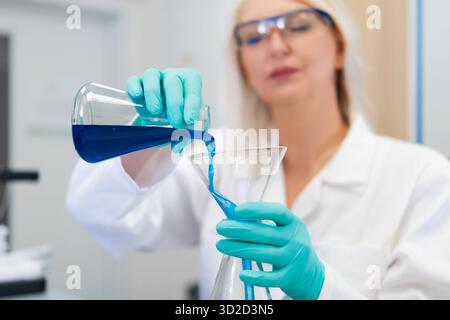 Woman scientist using a glass funnel to pour liquid solution in a laboratory. Represents accuracy, research, chemistry, and modern scientific techniques in laboratory work. Stock Photo