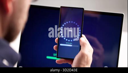 Man At Workplace Installing Software Update Progress On Smart Phone. Male Engineer Loading Patch From Internet Stock Photo