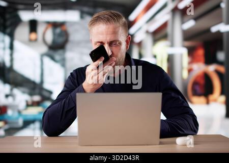 Male Businessman In Hotel Lobby Using Phone And Laptop Simultaneously. Stock Photo
