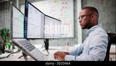 Young African American Man Using Laptop To Review Multiple Invoices. Stock Photo