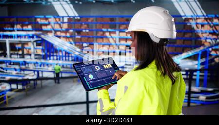 Female Logistic Technician Ensures Safety With Warehouse Automation Software Dashboard Stock Photo