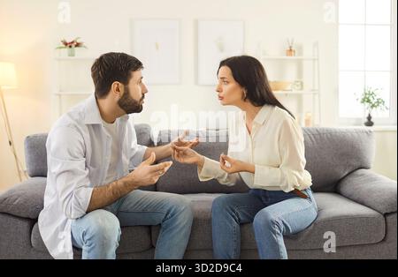 Angry couple conflict at home, young man, woman sitting on sofa in living room having family talk Stock Photo