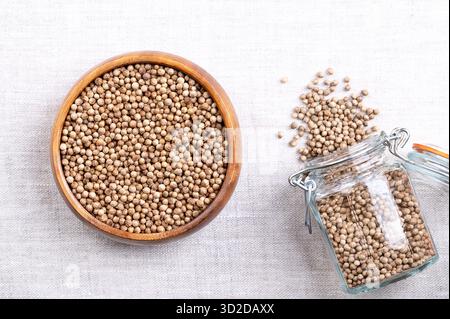 Whole and dried coriander seeds, in a wooden bowl on linen. Fruits of Coriandrum sativum, used as spice, with lemony citrus flavor. Stock Photo
