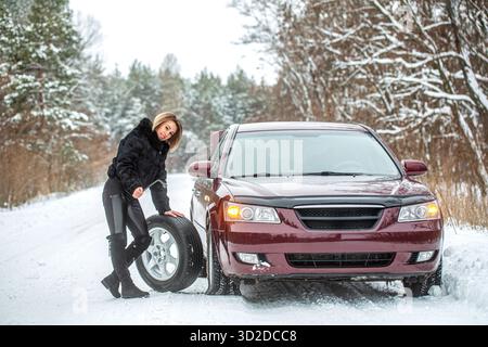 Female using changing wheel. Woman changing the punctured tyre on his car in winter. Pretty girl replacing tyres. Fault car in the winter. Girl trying Stock Photo