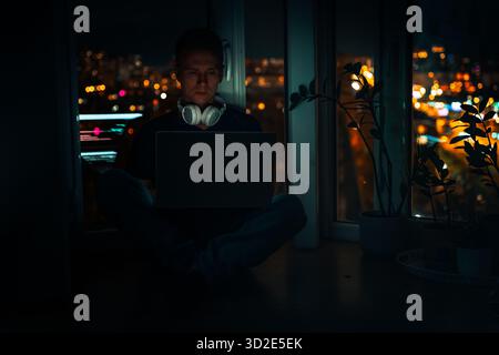 A young male developer is programming a code script late at night with beautiful city lights at night. Stock Photo