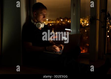 A young male developer is programming a code script late at night with beautiful city lights at night. Stock Photo