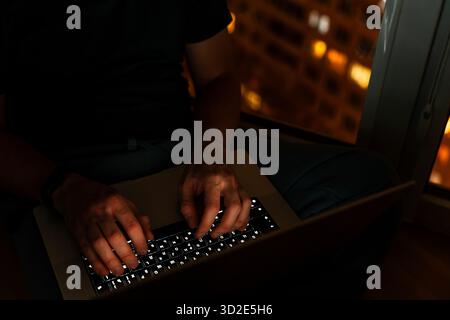 Programmer's hands are coding on a laptop in the dark with a view of the lights of the night city. The concept of a developer or hacker. Stock Photo