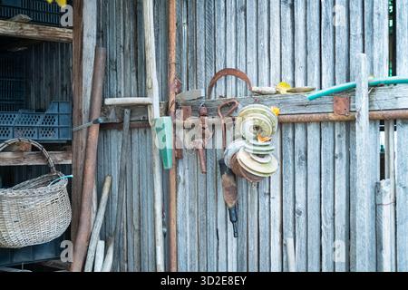 Rustic wooden shed wall with hanging tools and gardening equipment in an outdoor workshop Stock Photo