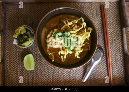 Savory Khao Soi, northern Thai noodle soup. An appetizing, comforting bowl of yellow curry with egg noodle, crispy topping, and lime on traditional wo Stock Photo