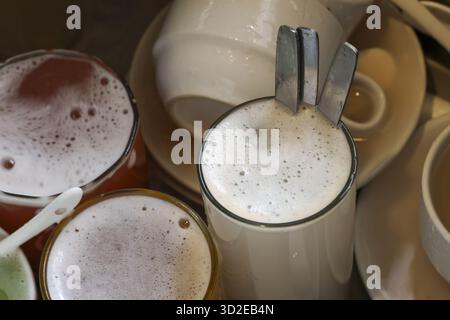 Messy pile of dirty dishes, including glass, cup, and spoon, waiting in sink. aftermath of meal creates feeling of necessary chore and domestic untidi Stock Photo