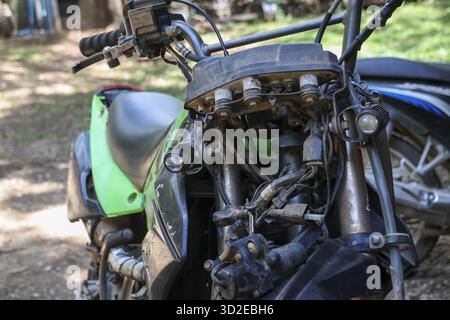 Close up view of green dual sport motorcycle undergoing maintenance and repair. Exposed wiring on engine and handlebar show custom bike project in an Stock Photo