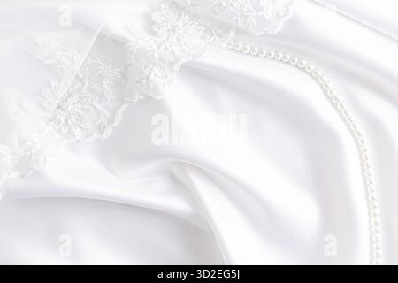 Delicate texture of the background. Elegant soft satin fabric in white with waves and part of the bride's lace veil. Wedding background Stock Photo