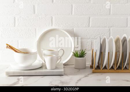 A set of kitchen utensils on a white marble countertop, a dryer with plates against the background of a white brick wall. ecologically clean house Stock Photo