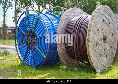 wo large reels with blue and black coiled cables standing on grass, prepared for infrastructure underground electricity installation, energy infrastru Stock Photo