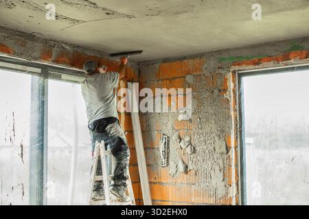Two construction workers plastering and leveling the ceiling during interior renovation in a building with brick walls. Professional builders working Stock Photo