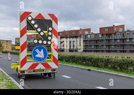 A yellow arrow board trailer on a street in the Netherlands, displaying a downward-right arrow for traffic diversion near modern apartment buildings. Stock Photo