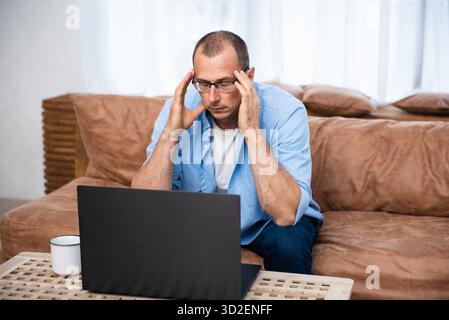 Handsome young man sitting on the couch and working on laptop computer, working remotely from home. Social distancing Self Isolation || Model released Stock Photo