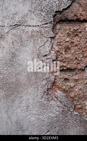 Close-up of an old concrete wall with deep cracks and worn cement revealing reddish brick beneath. Suitable for grunge design, abandoned structures, h Stock Photo