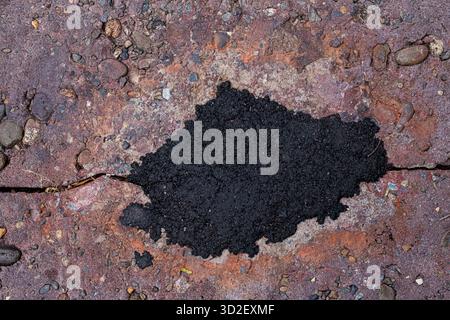Close-up view of a cracked terracotta colored concrete surface and a small pile of asphalt. Rough, distressed texture ideal for wallpaper and backgrou Stock Photo