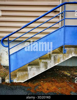 Concrete stairs are featured prominently, adorned with a bright blue railing. The setting appears industrial, with a textured wall in the background a Stock Photo
