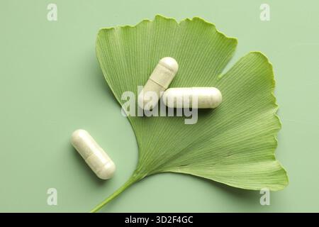 Ginkgo biloba leaf and pills on green background, flat lay Stock Photo