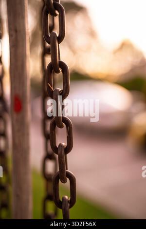 Metal chain links hanging vertically, displaying strength and connection at close range against a soft bokeh background of an outdoor golden hour scen Stock Photo