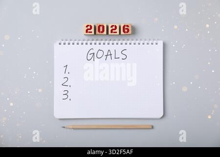 New 2026 Year Goals. Inscription in notebook and cubes with numbers on light grey background, top view. Bokeh lights Stock Photo