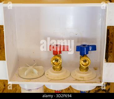 Closeup of hot and cold water connections and drain connection in a hard plastic housing, for washing machine, installed on the wall of a new laundry room construction Stock Photo