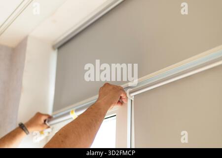 Male hands installing window blinds on modern window indoors. Stock Photo