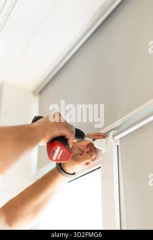 Male hands holding screwdriver while installing foil roller blinds on window frame. Stock Photo