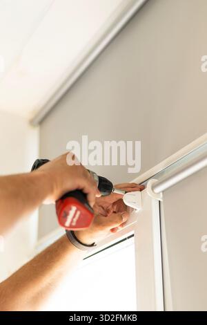 Close up of male hands with screwdriver installing roller blinds on window indoors. Stock Photo