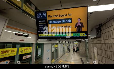 BUSAN, SOUTH KOREA - OCTOBER 10, 2025 - Subway platform display screen showing train arrival, Dadaepo Beach destination, and sign language interpreter Stock Photo
