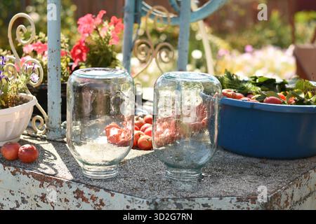 Two clean upside-down glass jars on a well, next to tomatoes, greens, and a blue bowl outdoors Stock Photo