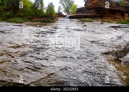 Shallow water cascades across smooth textured rock in Zion National Park creating flowing patterns & reflective highlights in a peaceful natural scene Stock Photo