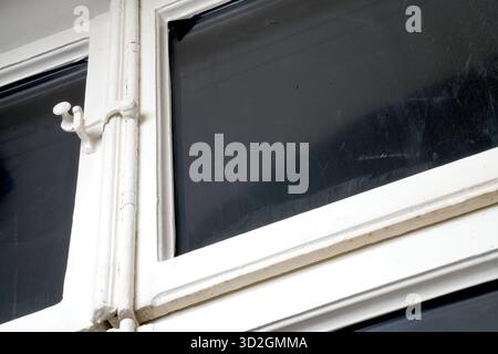 Macro shot of a detail of an old wooden window, painted white, with visible signs of wear and cracked paint. Focus on the vintage metal hook latch. Stock Photo