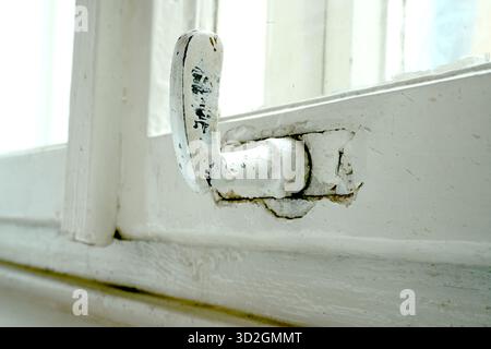 A macro shot of an old, curved window handle with cracked white paint. An image of a detail of an old wooden window frame, Stock Photo