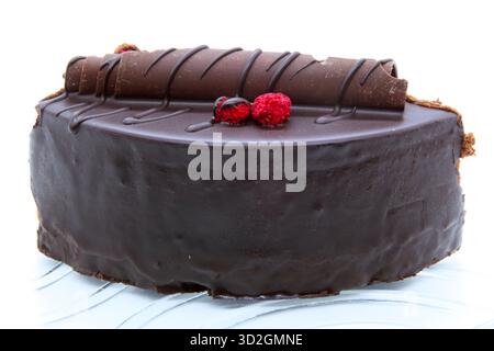 Close-up of a delicious slice of dark chocolate cake covered with glossy frosting. The dessert is decorated with chocolate curls and fresh raspberries Stock Photo