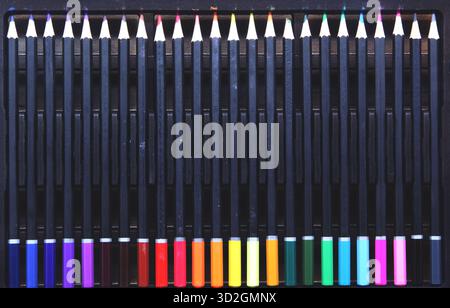 Top view of a complete set of colored pencils with black barrels, neatly arranged in a pencil case. The pencils are arranged in a color gradient, emph Stock Photo