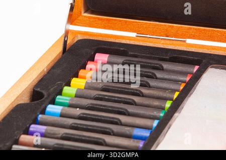 Close-up of a set of bright, square pastel crayons arranged by color in the compartments of a black tray inside an open wooden case. Stock Photo