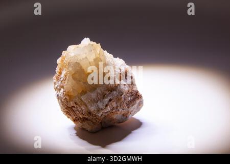 Close-up of an uncut piece of rock or crystal with yellowish-beige crystalline facets. The stone is brightly lit from below or from the side. Stock Photo