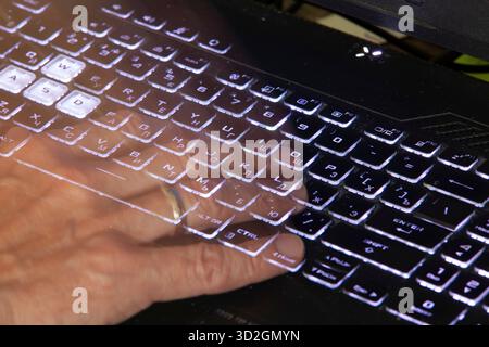 Close-up of a hand pressing the Home key on a black laptop keyboard with white backlighting. The keyboard contains Russian and English characters. Stock Photo