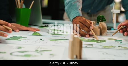A dynamic workspace showcases hands of diverse individuals engaged in analyzing and sketching sustainable design concepts, emphasizing teamwork and ec Stock Photo