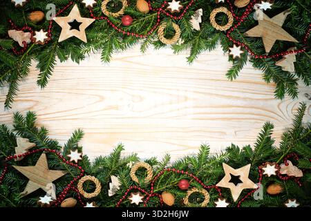 Christmas holiday background with top and bottom borders from fir tree branches, wooden stars, walnuts, cookies and more decoration on light rustic wo Stock Photo