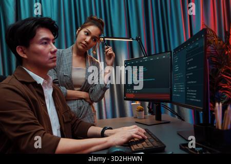 IT developers discussing with point to intelligent website development coder system running data online two screens information technology at neon lig Stock Photo