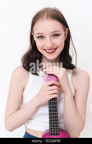 Portrait of happy woman ukulele artist holding ukulele, toothy smiling and gazing at camera with real facial expression. 18 year old authentic woman C Stock Photo