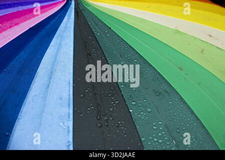 Vibrant rainbow umbrella fabric, glistening with fresh rain droplets, creates cheerful and protective scene. colorful spectrum offers bright perspecti Stock Photo